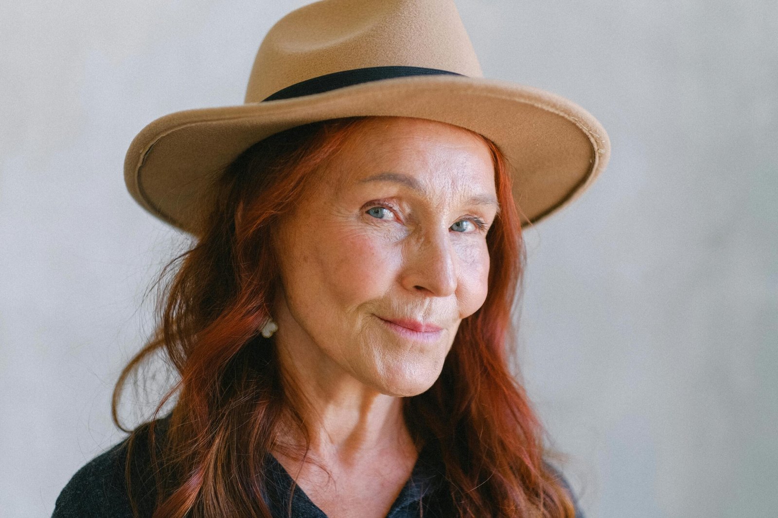 Charming senior woman with red hair and beige hat smiling confidently.
