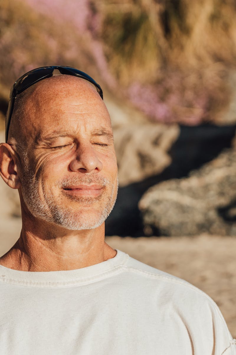 Content senior man with eyes closed, meditating and relaxing on a sunny beach day.