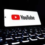 YouTube app icon displayed on a smartphone over an illuminated keyboard, representing digital media and online streaming.